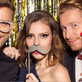 Three people having fun with photo booth props, including glasses, a mustache, and lips